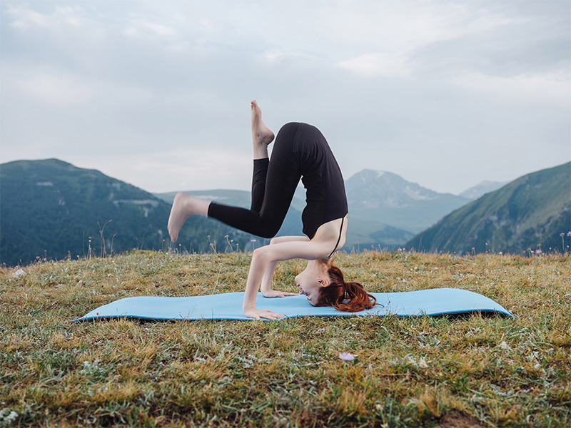 A woman performing an inverted yoga pose, surrounded by nature. Strong, focused, and determined, mat on grass.