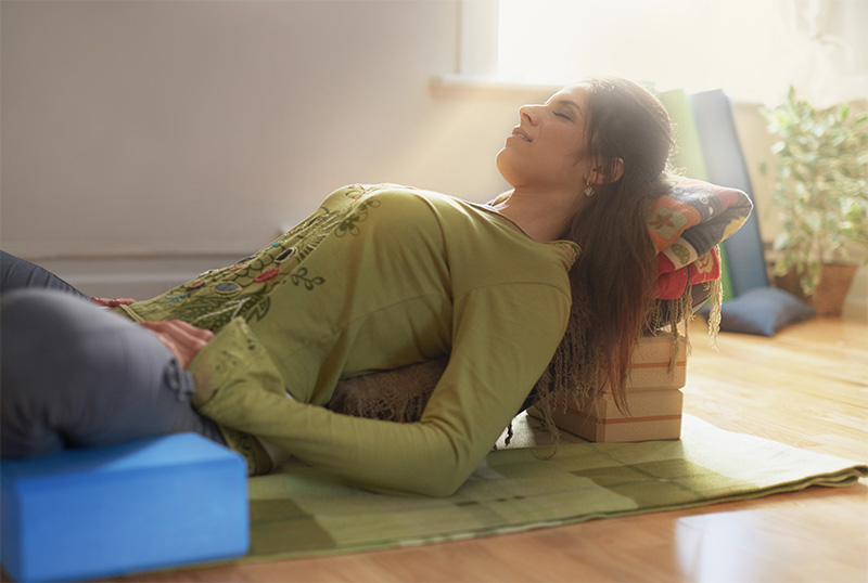 Woman in restorative yoga pose on incline surface.