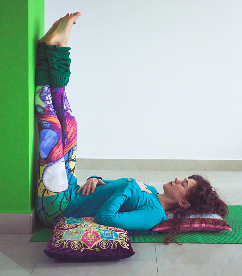 Young woman relaxing in yoga pose with legs up against a wall.